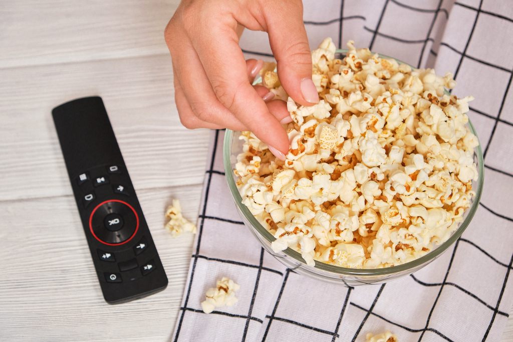 hand grabbing popcorn from a bowl next to a tv remote