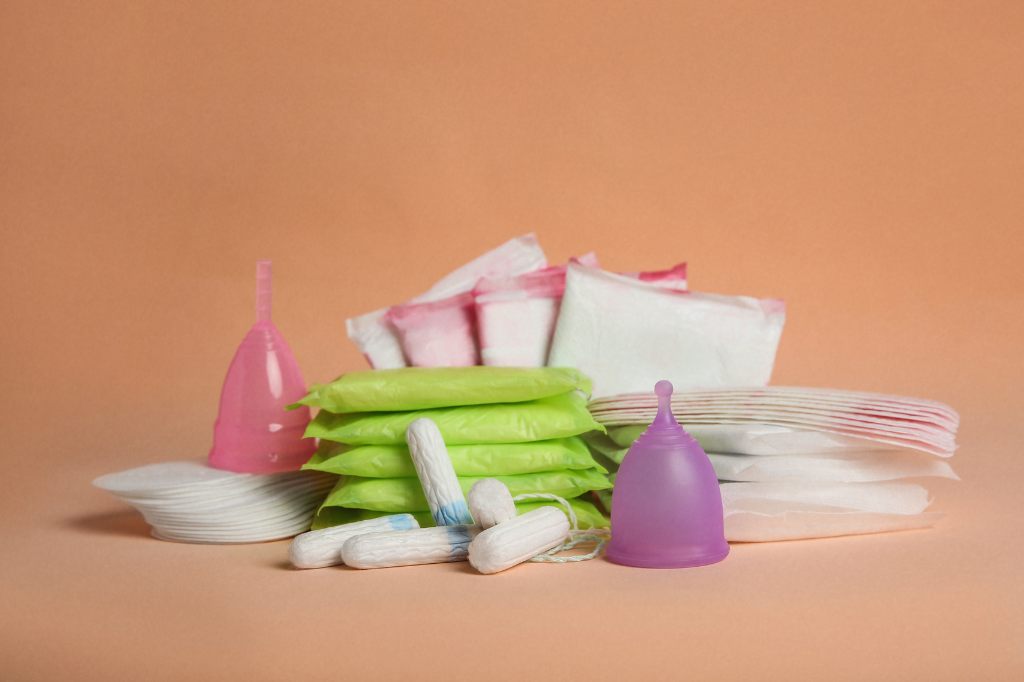 pile of period products including menstrual cups, pads, pantiliners, and tampons